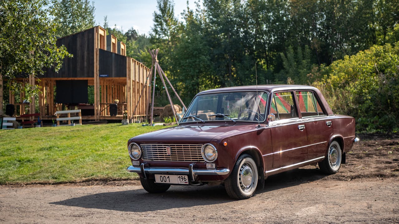A classic maroon sedan parked outdoors in Сысерть, Russia, with a rustic backdrop.