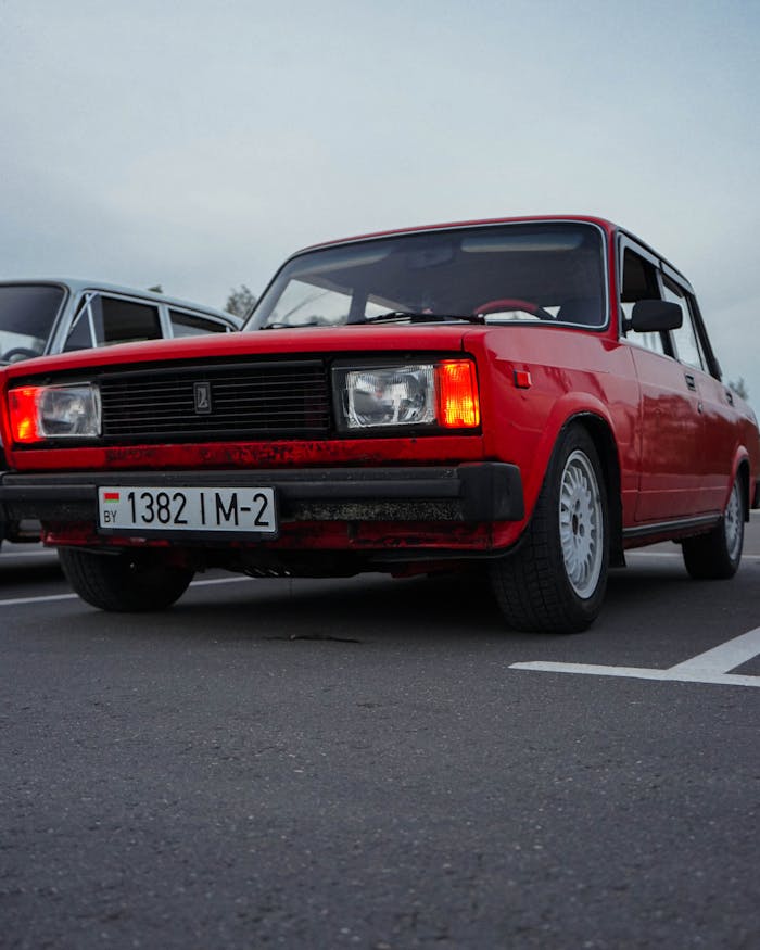 Classic red car parked on pavement with headlights on, capturing a vintage style in twilight.