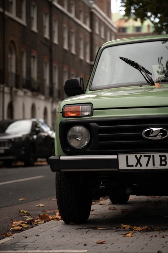 Close-up of a green Lada Niva parked on a city street with falling leaves.