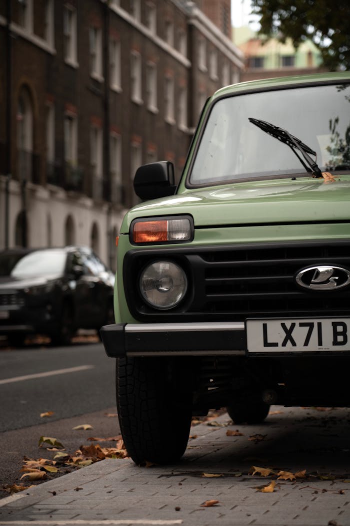 Close-up of a green Lada Niva parked on a city street with falling leaves.